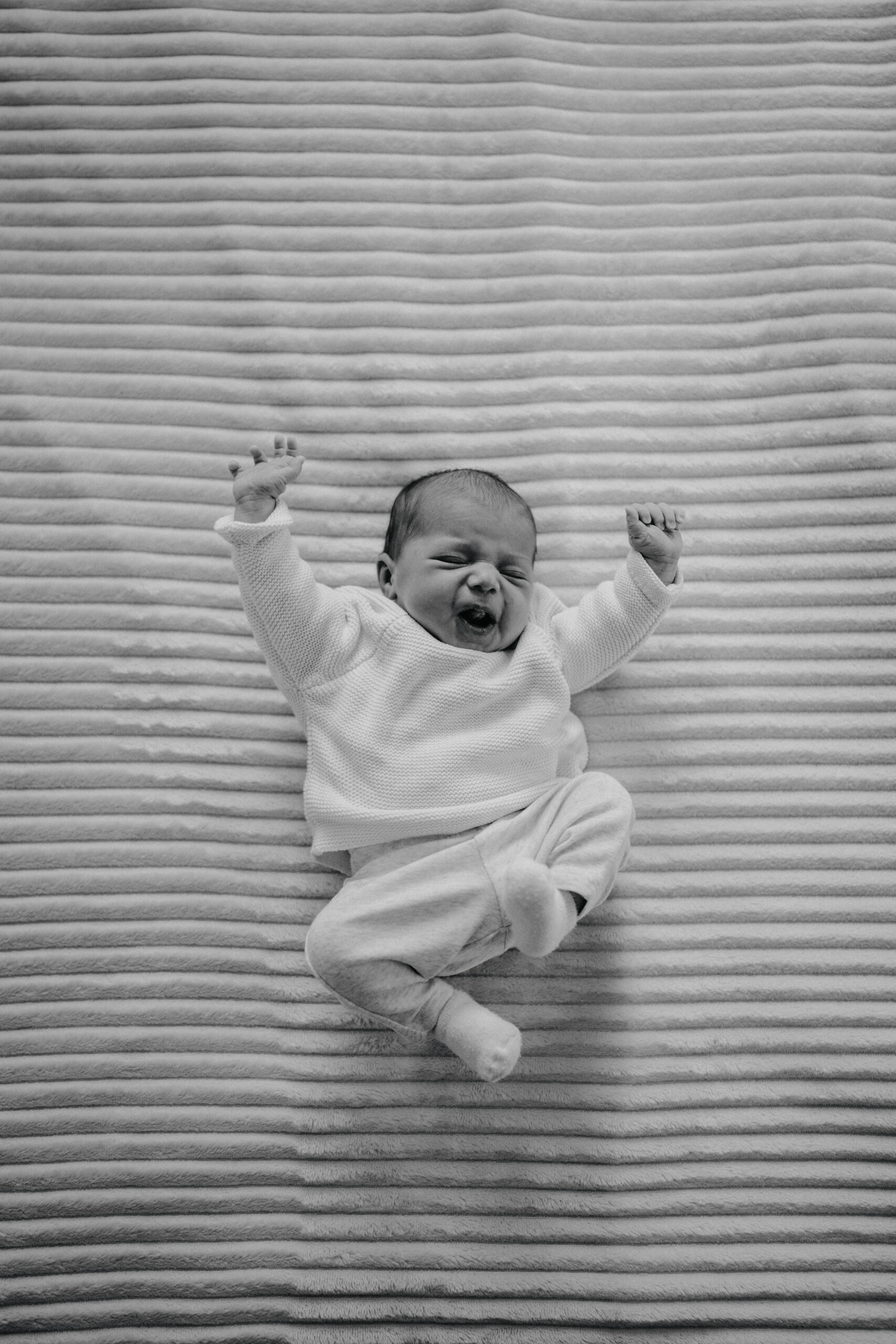 Nouveau-né s'étirant sur un plaid lors d'une séance photo naissance en noir et blanc.