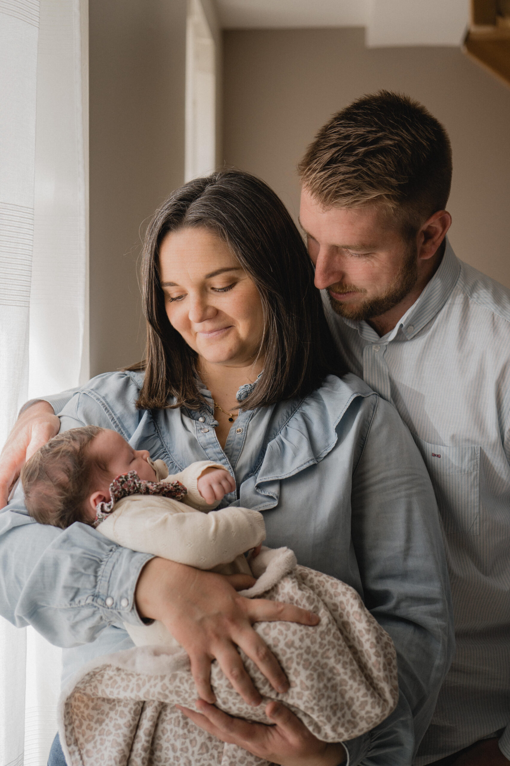 Jeunes parents admirant leur nouveau-né dans leurs bras pendant une séance photo à domicile.