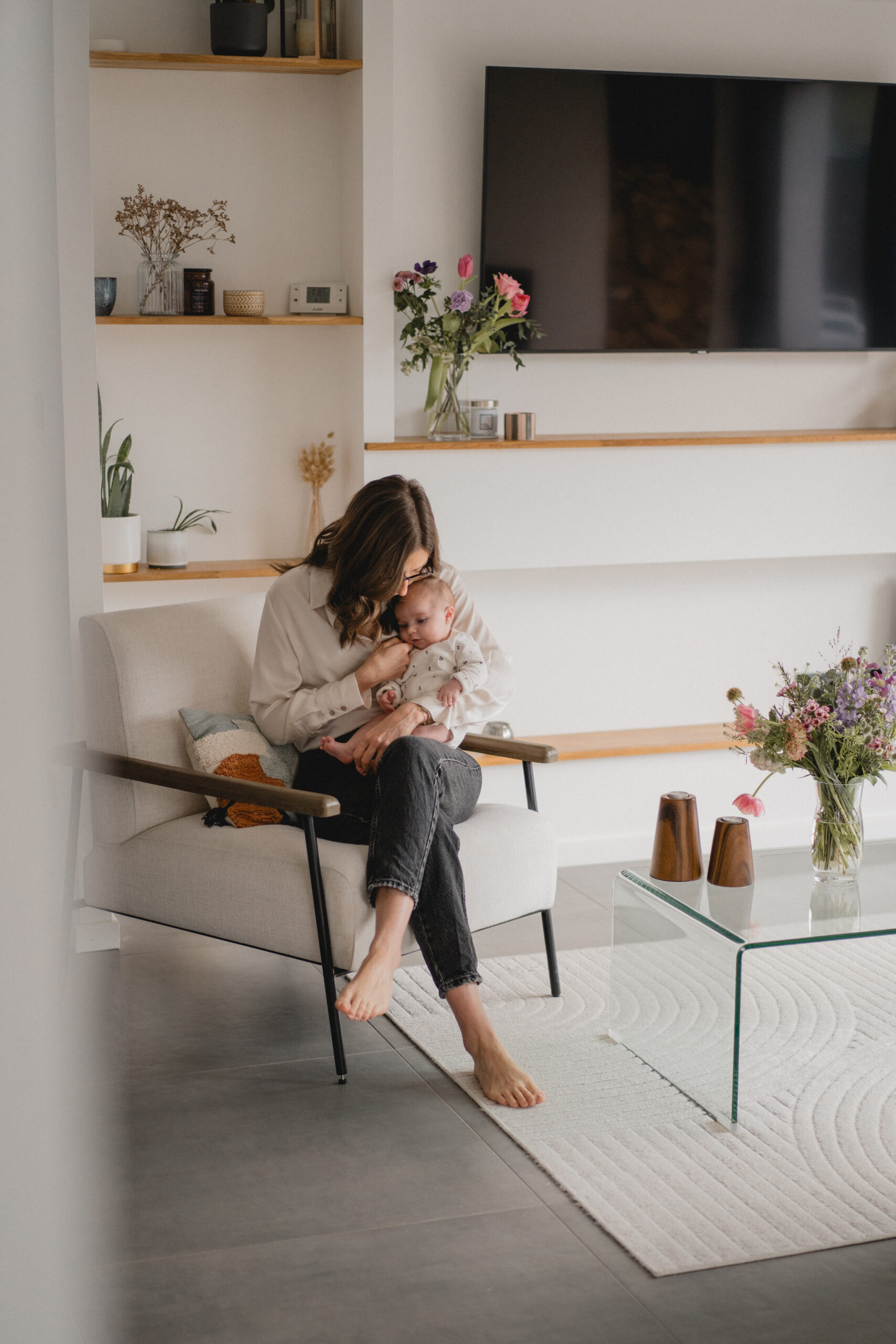 Jeune maman berçant son nouveau-né dans son salon lors d'une séance photo naissance.