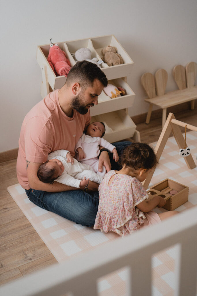 Jeune papa entouré de ses trois enfants dont ses nouvelles jumelles pendant une séance photo famille à domicile