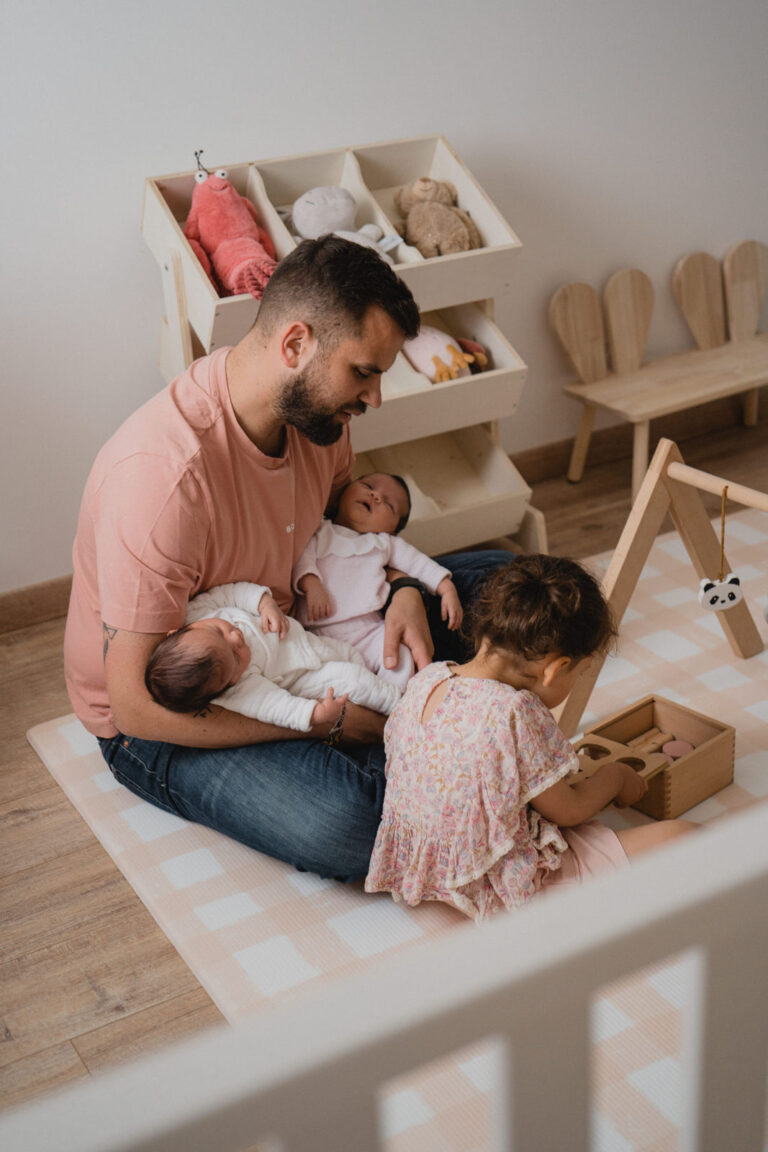 Jeune papa entouré de ses trois enfants dont ses nouvelles jumelles pendant une séance photo famille à domicile
