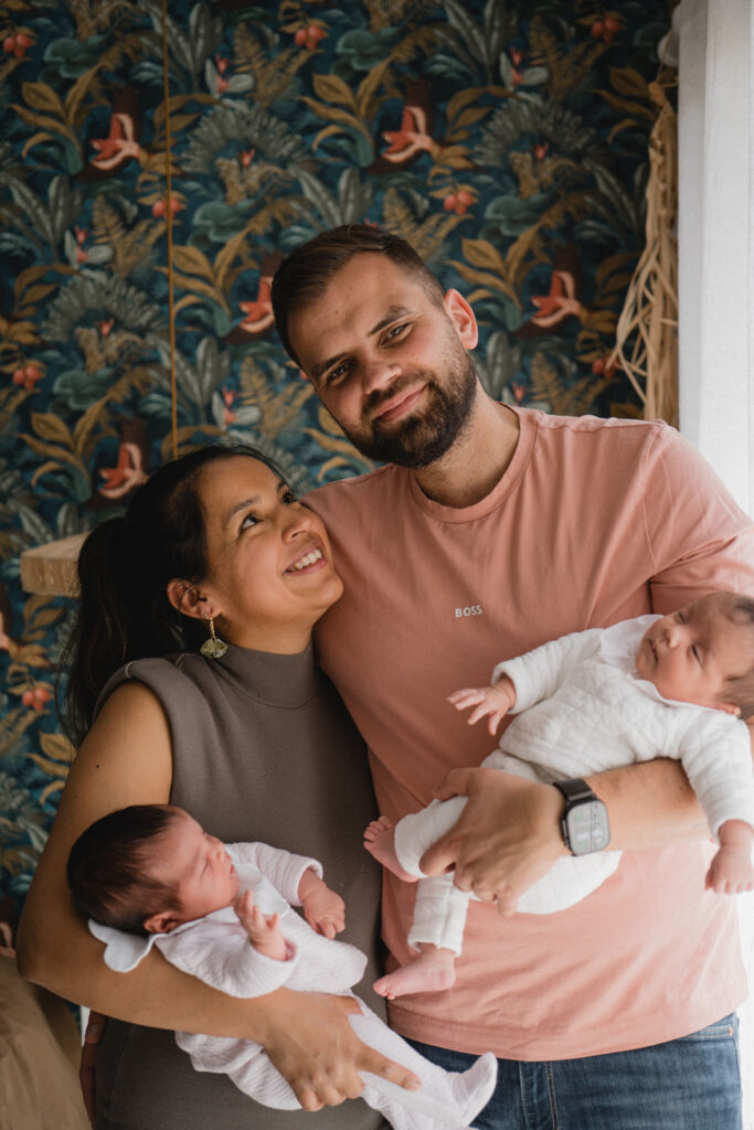 Jeunes parents tenant leurs jumelles nouveau-nées lors d'une séance photo naissance à domicile.