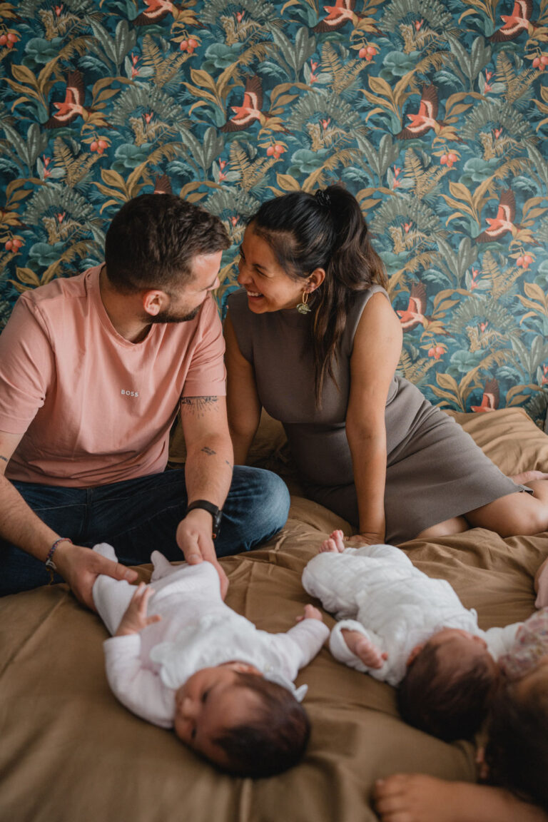 Les parents échangent un regard complice et rieur devant leur deux jumelles nouvellement nées.