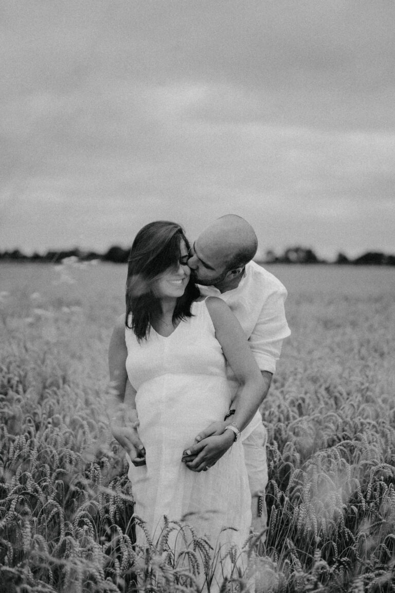 Portrait en noir et blanc d'une future maman et de son compagnon dans un champ de blé.