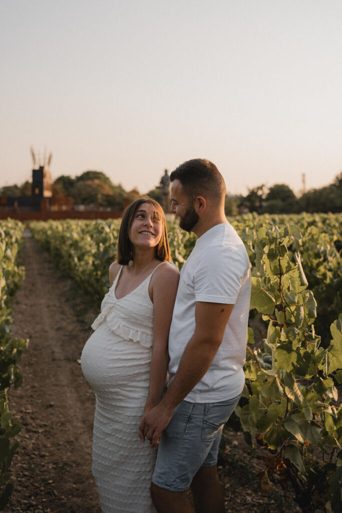 Future maman et futur papa souriants dans les vignes au coucher du soleil.