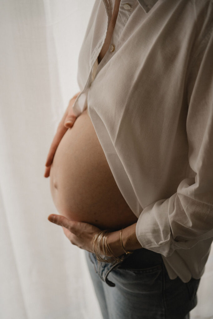 Gros plan sur le ventre d'une femme enceinte caressé avec douceur pendant une séance photo.