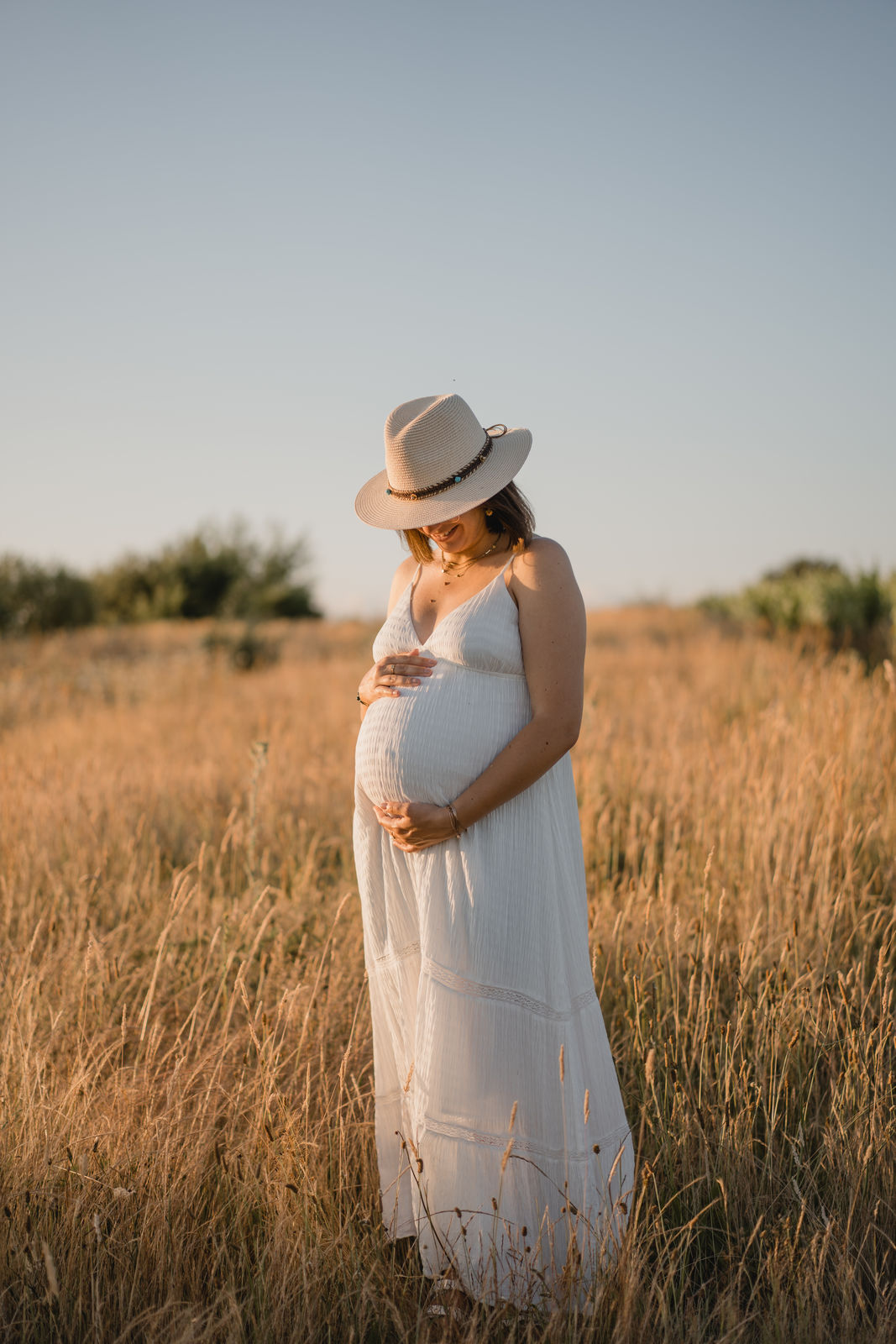 Future maman en robe blanche dans un champ doré au coucher du soleil.