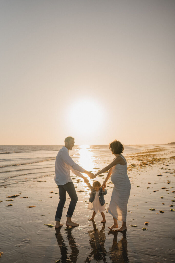 Famille jouant au bord de l'océan au coucher du soleil lors d'une séance photo en extérieur