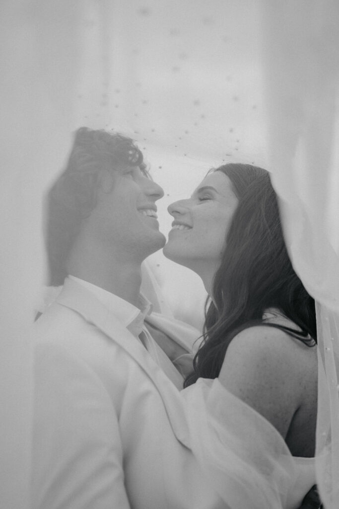 Les mariés se sourient derrière le voile de la mariée.