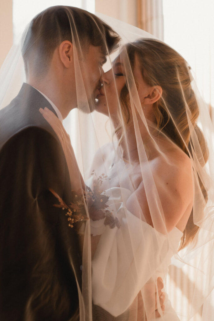Jeunes mariés s'embrassant tendrement sous le voile lors de leur mariage