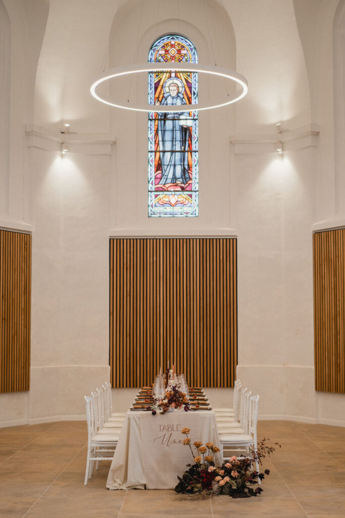 Table de réception installée dans une chapelle désacralisée baignée de lumière naturelle.