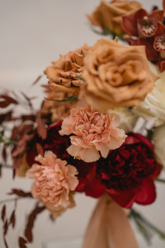 Gros plan sur un bouquet de mariée aux teintes terracotta, crème et bordeaux.