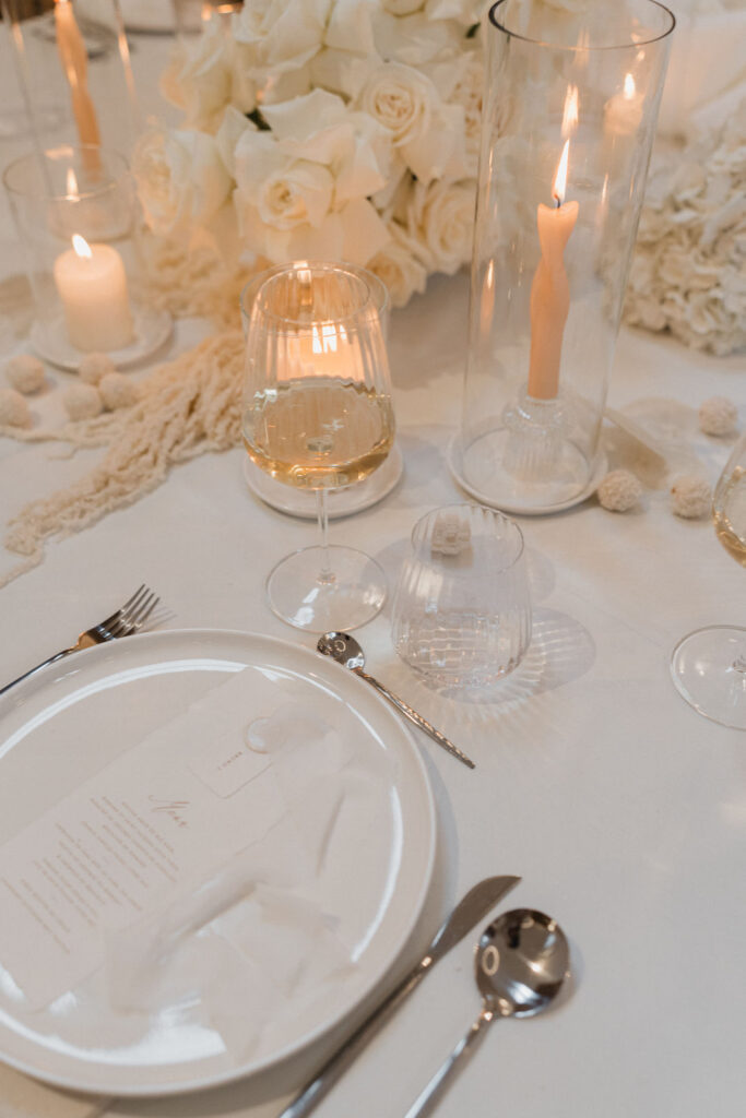 Détail de la décoration de table avec bougies, fleurs et vaisselle aux tons crèmes.
