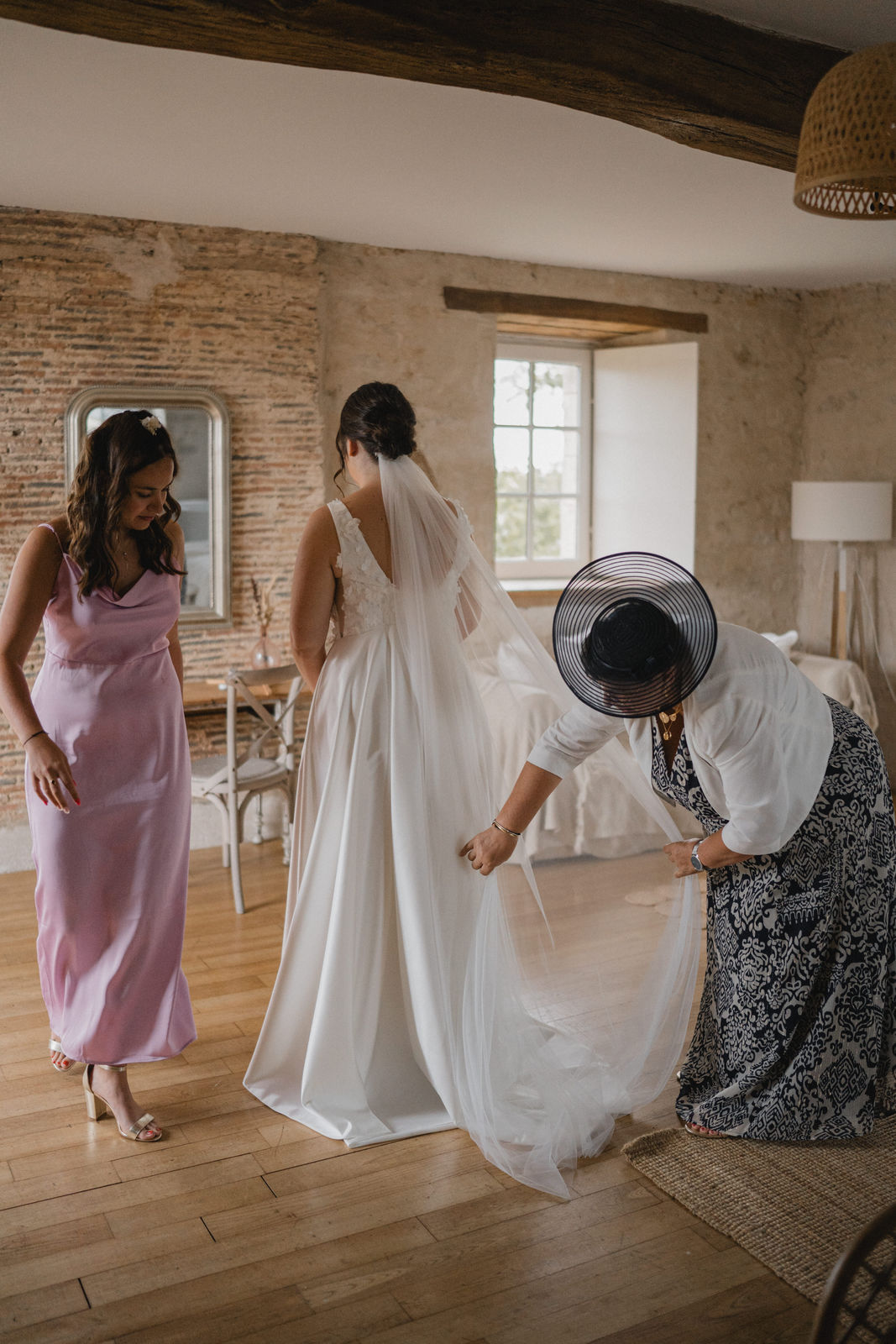 La mariée ajuste sa robe avec ses proches pendant les préparatifs.
