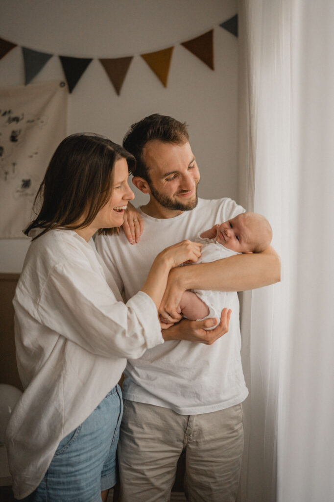 Jeunes parents admirant leur nouveau-né pendant une séance photo naissance à domicile.