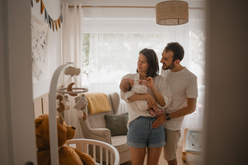 Jeunes parents tenant leur nouveau-né dans sa chambre lors d'une séance photo naissance.