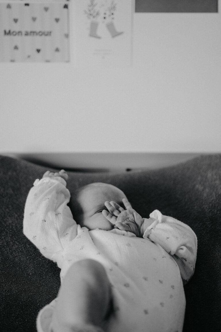 Nouveau-né s'étirant sur un canapé pendant une séance photo naissance en noir et blanc.