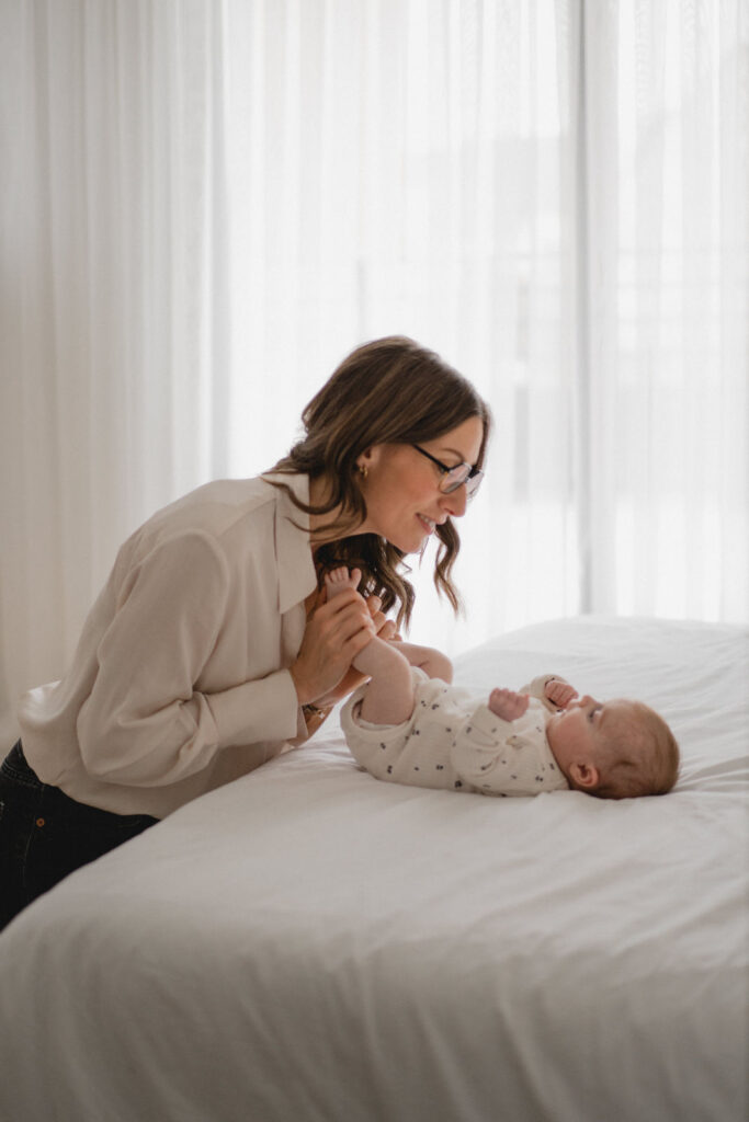 Jeune maman jouant avec son nouveau-né pendant une séance photo naissance à domicile.
