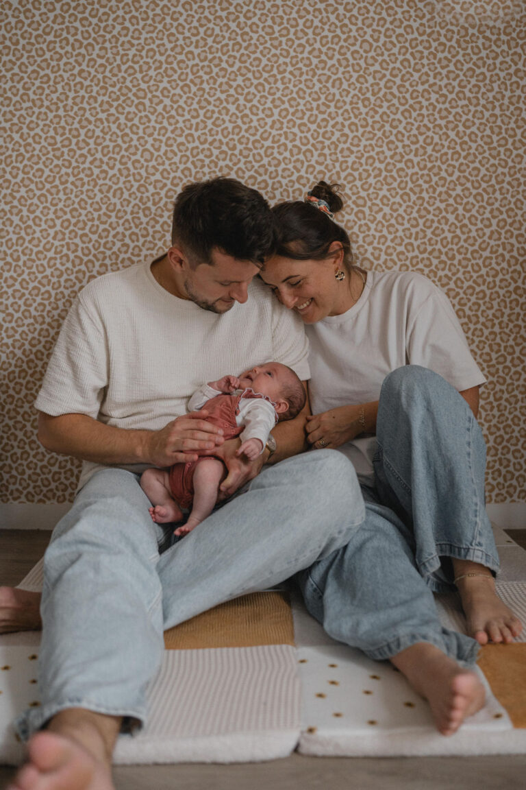 Jeunes parents regardant tendrement leur nouveau-né installé entre eux sur le tapis d'éveil.