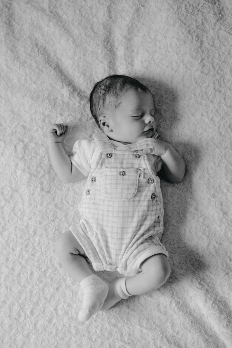 Nouveau-né endormi allongé sur une couverture pendant une séance photo naissance en noir et blanc.