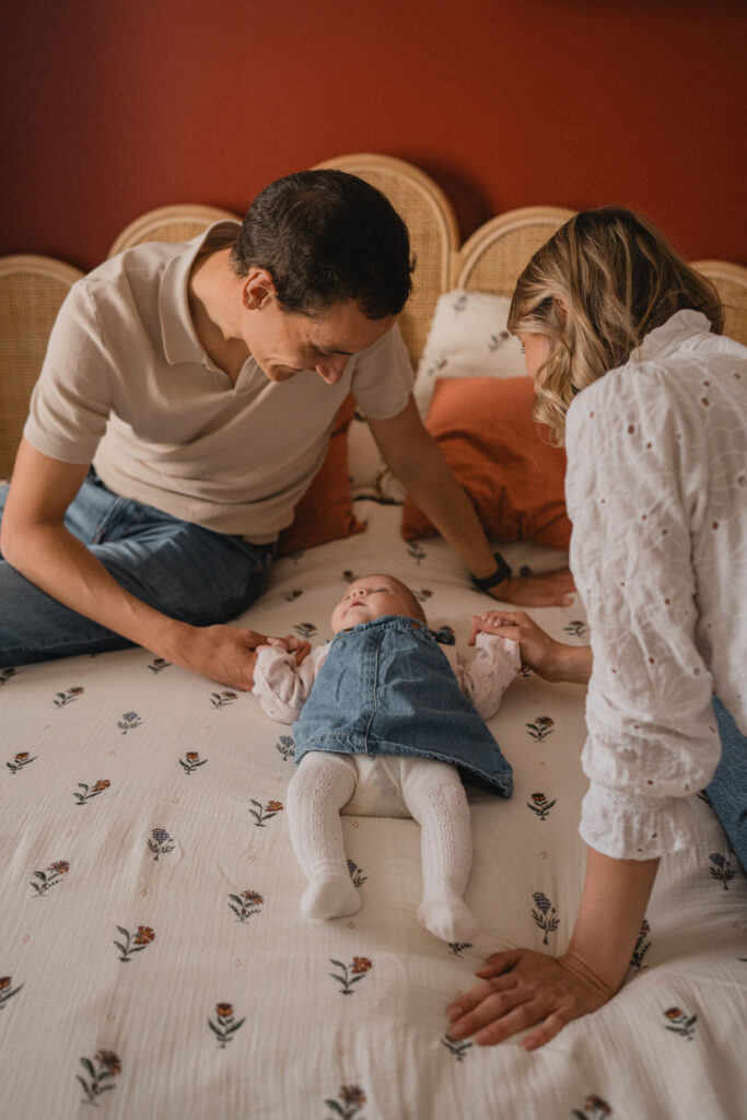 Jeunes parents admirant leur bébé allongé sur un lit pendant une séance photo à domicile.