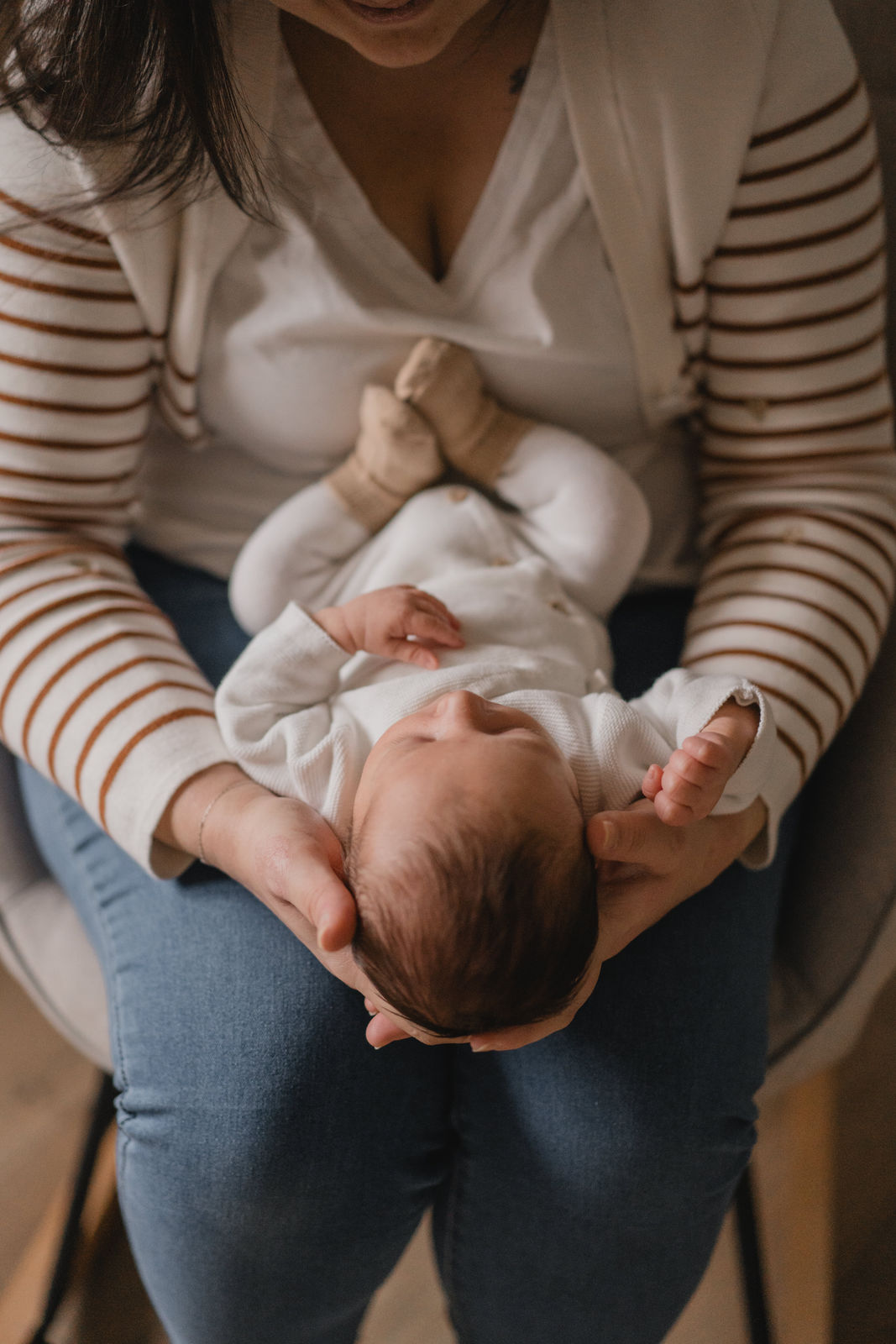 Jeune maman tenant son nouveau-né dans ses bras pendant une séance photo naissance à domicile.
