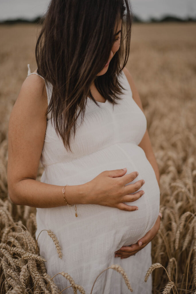 Portrait d'une future maman caressant son ventre au milieu d'un champ de blé.