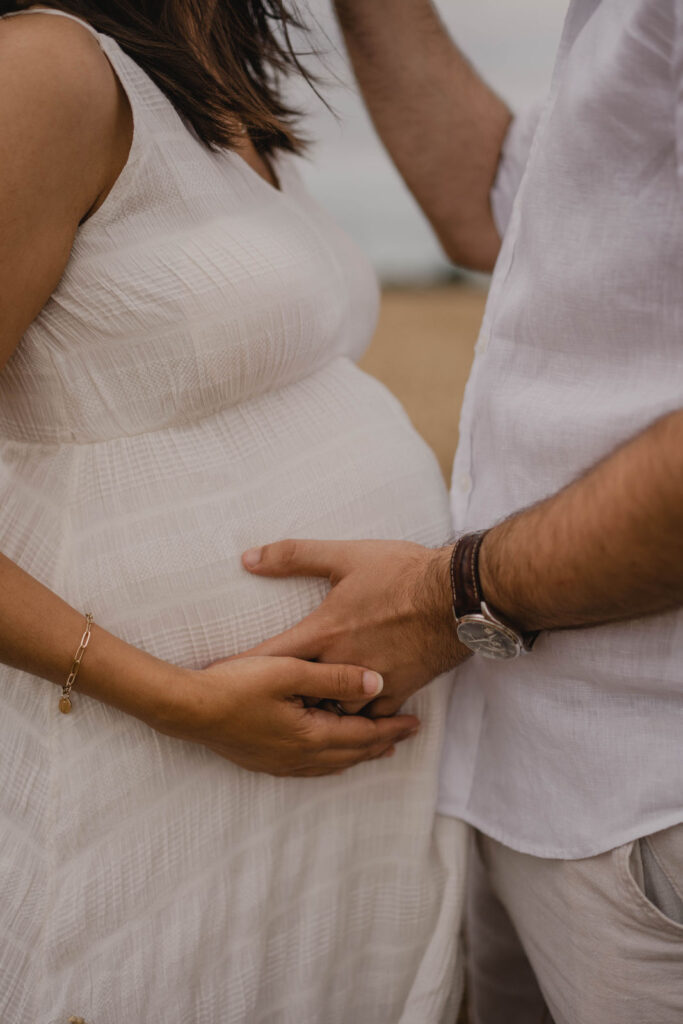 Gros plan sur les mains des futurs parents posées avec tendresse sur le ventre arrondi de la future maman.